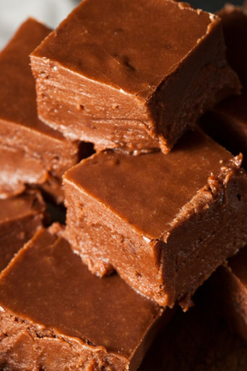 A stack of thick, creamy old-fashioned chocolate fudge squares on a cutting board