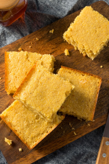 A fluffy square of golden cornbread on a cutting board.