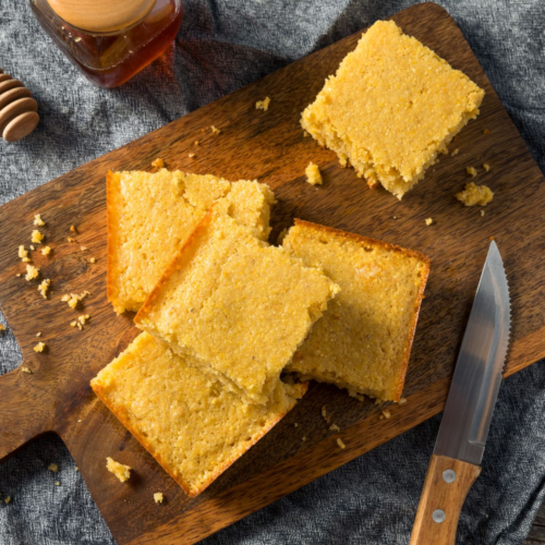 A fluffy square of golden cornbread on a cutting board.