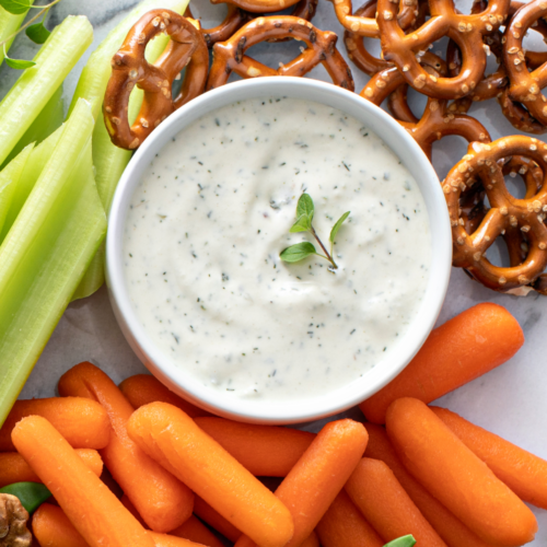 A jar of creamy homemade ranch dressing, sitting along side vegetables.
