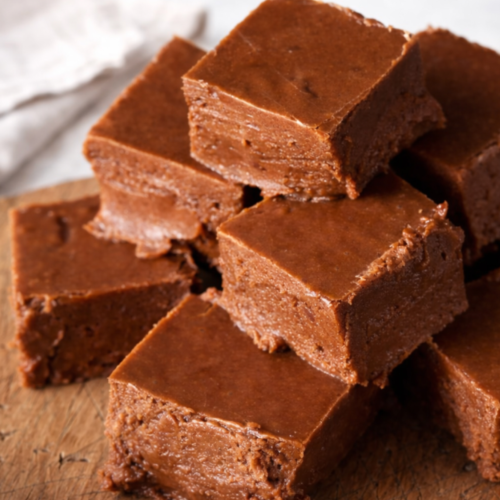 A stack of thick, creamy old-fashioned chocolate fudge squares on a cutting board.