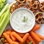A jar of creamy homemade ranch dressing, sitting along side vegetables.