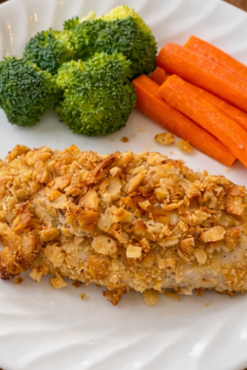 Crispy baked Ritz cracker chicken with a golden buttery coating, served on a plate with vegetables.