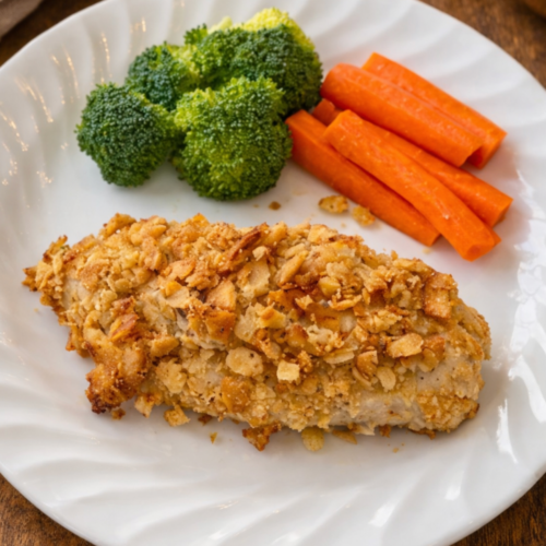 Crispy baked Ritz cracker chicken with a golden buttery coating, served on a plate with vegetables.