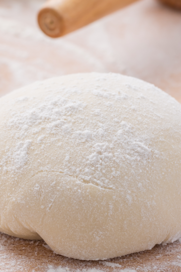 Pizza dough in a ball resting on a table top, ready to be rolled out and topped.