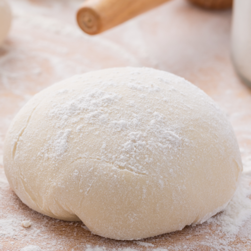 Pizza dough in a ball resting on a table top, ready to be rolled out and topped.