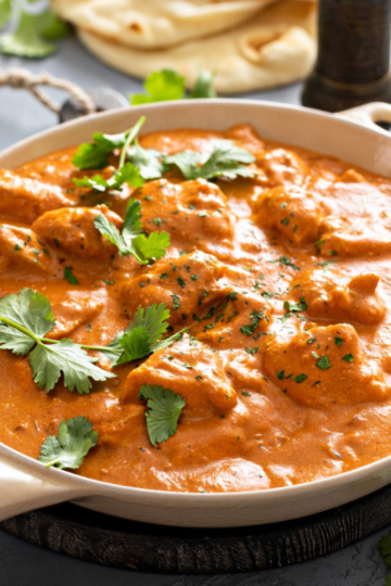 A bowl of creamy authentic Indian butter, chicken, garnished with fresh cilantro served with a side of fluffy naan.