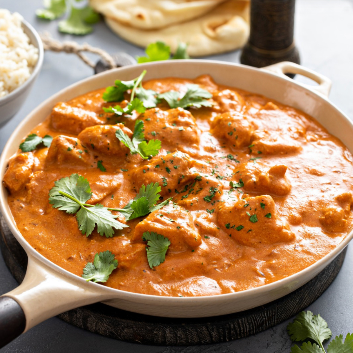 A bowl of creamy authentic Indian butter, chicken, garnished with fresh cilantro served with a side of fluffy naan.