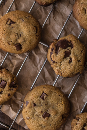 A cookie rack of eight gooey, golden brown butter chocolate chunk cookies on a rustic wooden board.