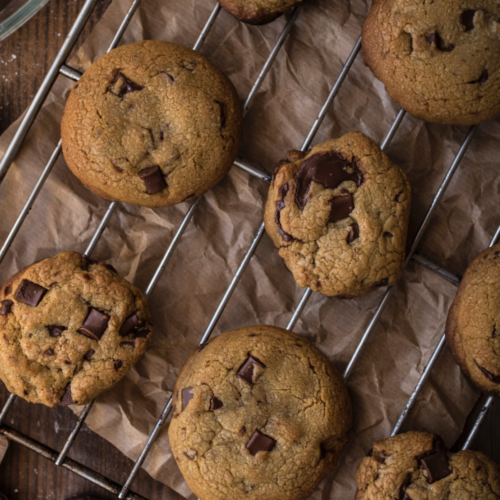 A cookie rack of eight gooey, golden brown butter chocolate chunk cookies on a rustic wooden board.