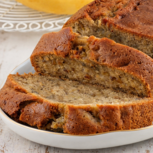 Slices of moist banana bread with a golden-brown crust, served on a white plate with a soft, tender crumb visible.