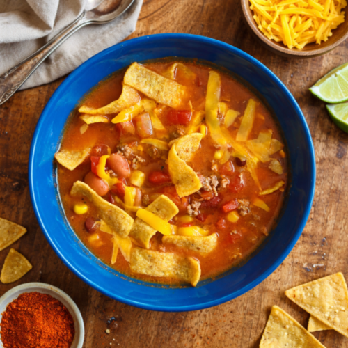 Bowl of hearty homemade chili topped with shredded cheese and tortilla chips on a rustic wooden table