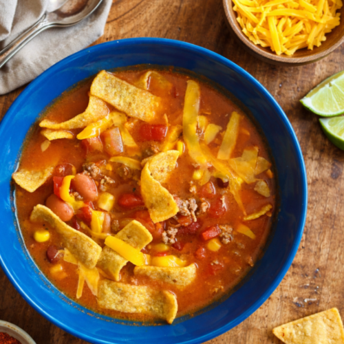 Bowl of hearty homemade chili topped with shredded cheese and tortilla chips on a rustic wooden table