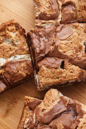 Layered brownie bars with a crackly chocolate top and gooey marshmallow and peanut butter center, cut into squares and served on a cutting board.