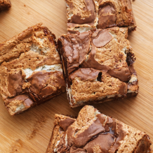 Layered brownie bars with a crackly chocolate top and gooey marshmallow and peanut butter center, cut into squares and served on a cutting board.