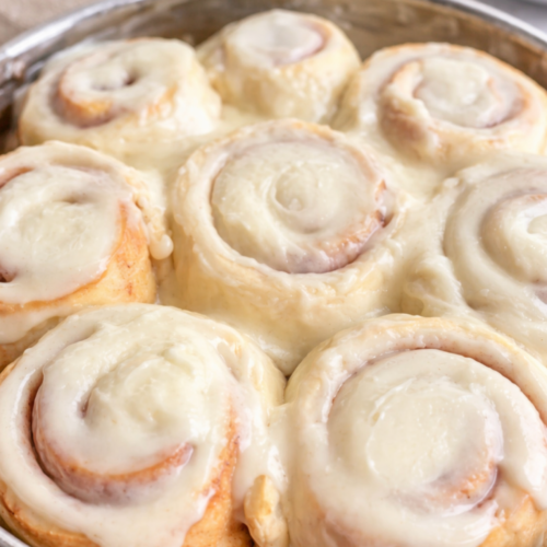 Soft 1-hour cinnamon rolls with creamy frosting on top, fluffy texture, and golden brown swirls in a baking dish.