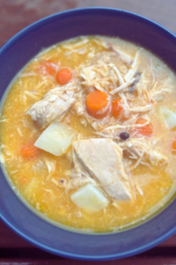 A bowl of homemade chicken soup with golden broth, tender shredded chicken, carrots, potatoes, and a rustic touch of sourdough discard for extra richness.