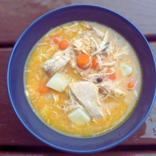 A bowl of homemade chicken soup with golden broth, tender shredded chicken, carrots, potatoes, and a rustic touch of sourdough discard for extra richness.