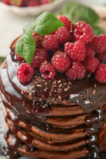 Stack of fluffy chocolate sourdough discard pancakes drizzled with glossy chocolate sauce and topped with fresh berries.