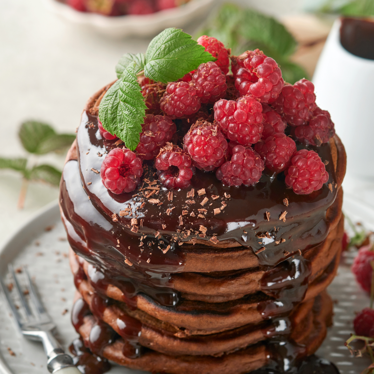 Stack of fluffy chocolate sourdough discard pancakes drizzled with glossy chocolate sauce and topped with fresh berries.
