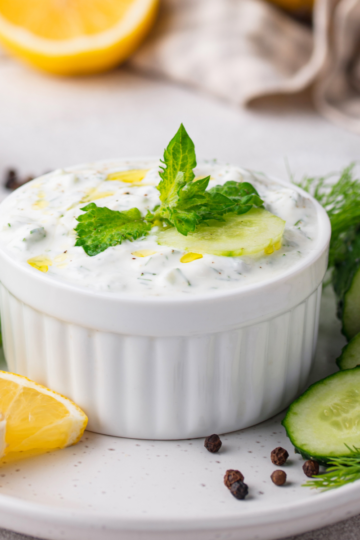 A bowl of creamy homemade garlic ranch dip topped with fresh herbs, surrounded by crisp vegetables for dipping.