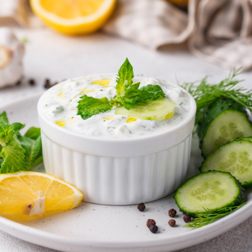 A bowl of creamy homemade garlic ranch dip topped with fresh herbs, surrounded by crisp vegetables for dipping.