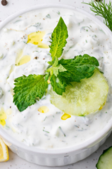 A bowl of creamy homemade garlic ranch dip topped with fresh herbs, surrounded by crisp vegetables for dipping.