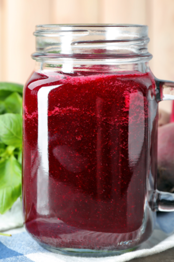 Fresh beet juice in a glass with vibrant red color, made from beets and served on checkered napkin.