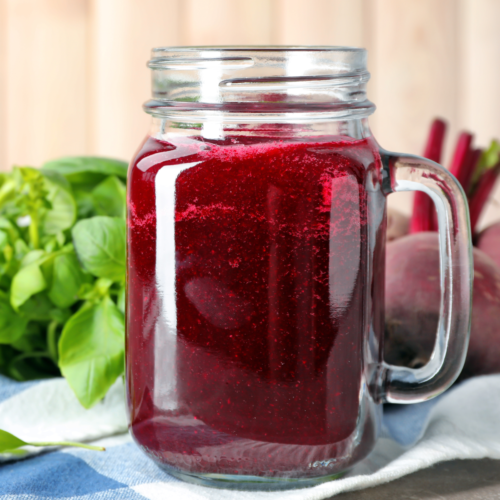 Fresh beet juice in a glass with vibrant red color, made from beets and served on checkered napkin.