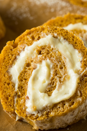 Brown Butter Pumpkin Roll with Maple Cream Filling dusted with powdered sugar and drizzled with maple syrup