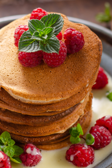 Stack of fluffy sourdough discard pancakes drizzled with creamy vanilla sauce and topped with fresh raspberries.