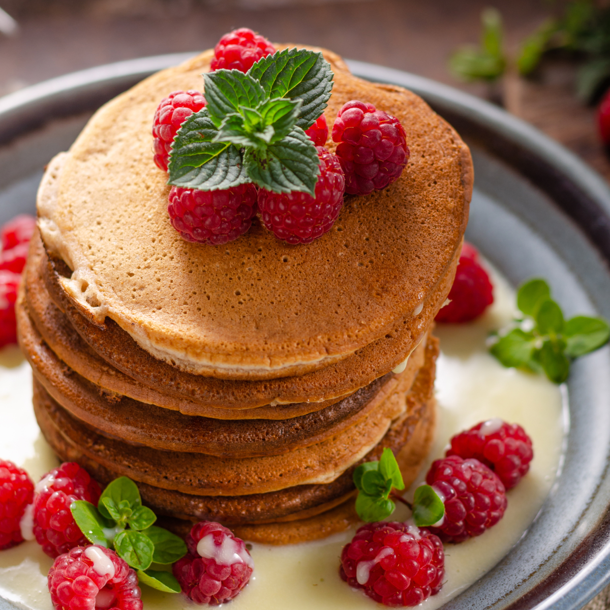 Stack of fluffy sourdough discard pancakes drizzled with creamy vanilla sauce and topped with fresh raspberries.