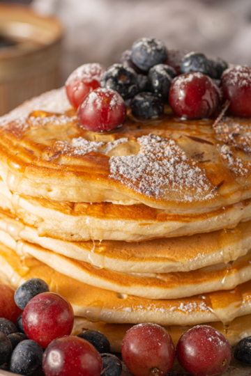 Fluffy sourdough discard pancakes stacked on a plate with fruit and syrup, golden brown and light in texture