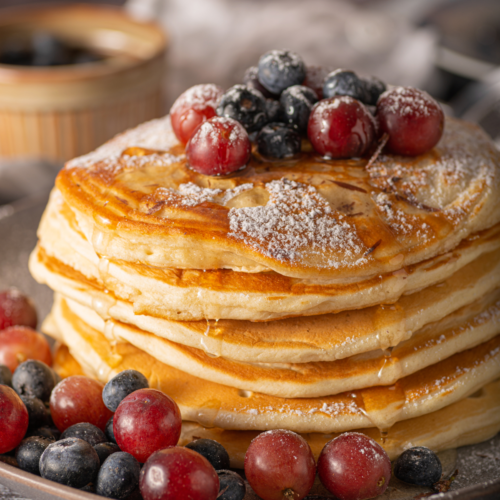 Fluffy sourdough discard pancakes stacked on a plate with fruit and syrup, golden brown and light in texture