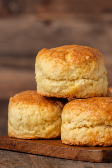 Freshly baked brown butter honey glazed biscuits on a cutting board, dripping with golden honey and melted butter