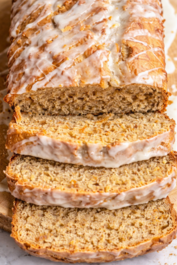 Sliced brown butter coconut banana bread drizzled with glaze on a wooden board, showing a moist, tender crumb