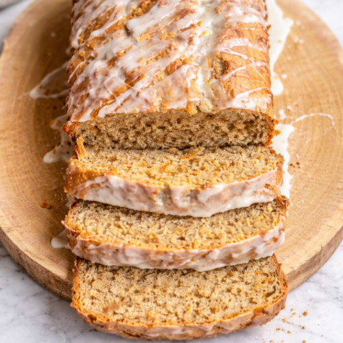 Sliced brown butter coconut banana bread drizzled with glaze on a wooden board, showing a moist, tender crumb