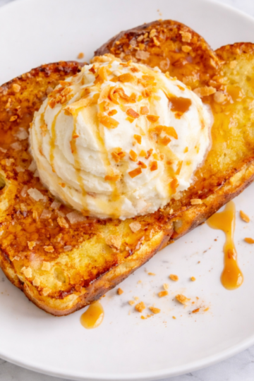 Thick slices of golden toasted coconut French toast topped with coconut whipped cream, toasted coconut flakes, and caramel drizzle.