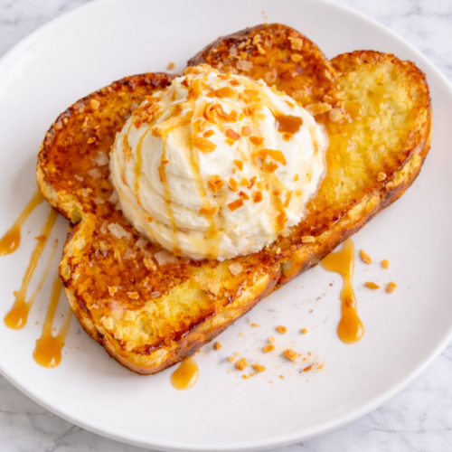 Thick slices of golden toasted coconut French toast topped with coconut whipped cream, toasted coconut flakes, and caramel drizzle.