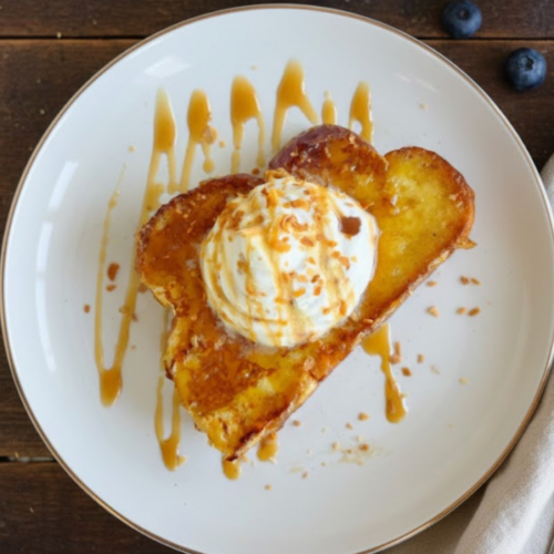 Thick slices of golden toasted coconut French toast topped with coconut whipped cream, toasted coconut flakes, and caramel drizzle.