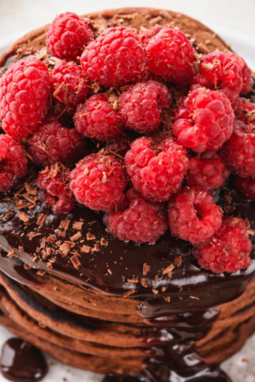 Stack of fluffy chocolate sourdough discard pancakes drizzled with glossy chocolate sauce and topped with fresh berries.