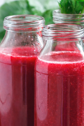 A glass of deep red beet juice with beet slices on a rustic wooden table.