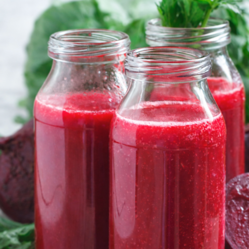 A glass of deep red beet juice with beet slices on a rustic wooden table.
