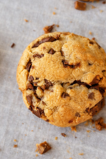 Close-up of thick, chewy brown butter toffee cookies with golden edges, soft centers, and melted chocolate chunks on parchment paper.