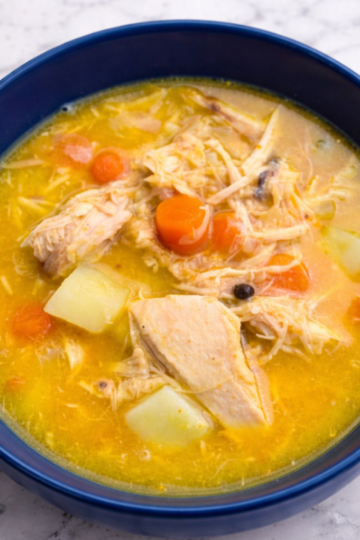 Bowl of hearty sourdough discard chicken soup with tender shredded chicken, carrots, potatoes, and rich golden broth on a marble countertop.