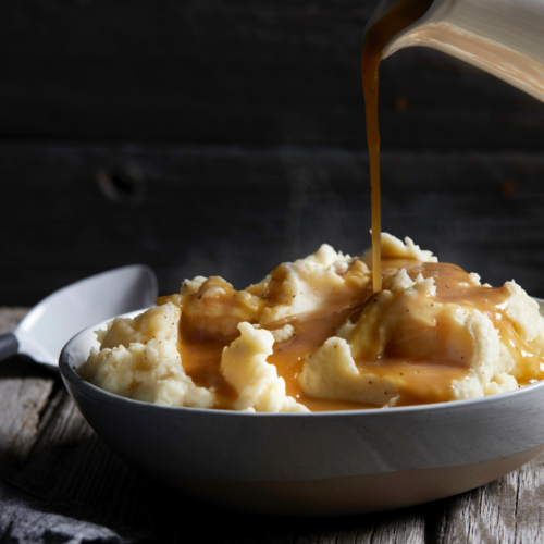 Rich, dark brown gravy made with sourdough discard, served in a white gravy boat and garnished with fresh thyme for a holiday meal.