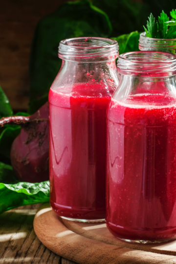 A glass of deep red beet juice with beet slices on a rustic wooden table.