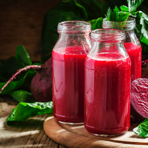 A glass of deep red beet juice with beet slices on a rustic wooden table.