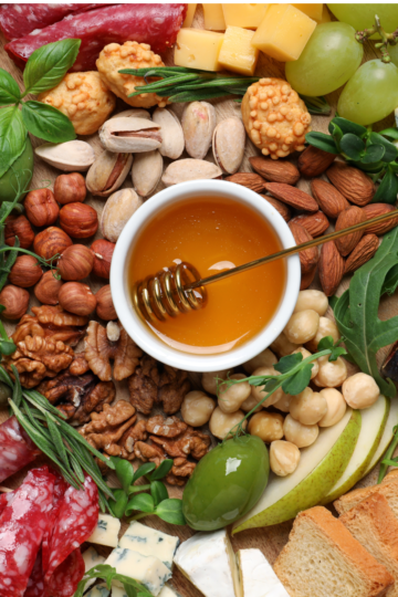 Savory charcuterie board with meats cheeses crackers and garnishes arranged on serving board.