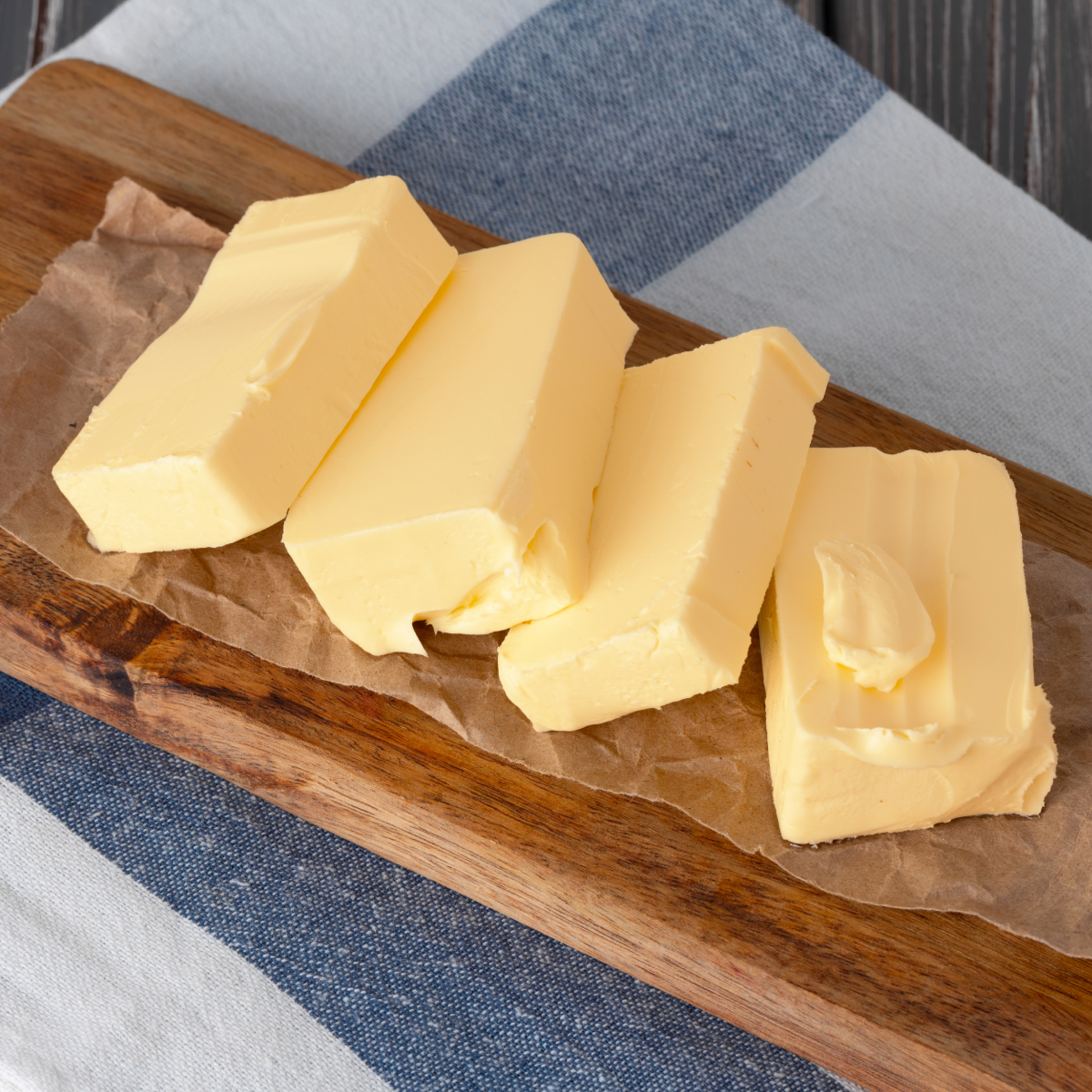 Slices of cold butter cut into sliced pieces on a wooden cutting board, ready to soften quickly for baking.